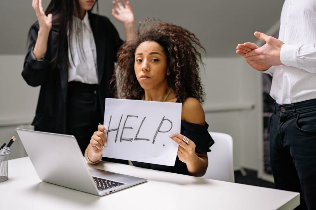 An unhappy businesswoman showing a sign reading 'HELP' in an office setting.